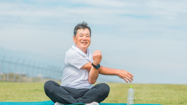 芝生でストレッチをしている60代男性